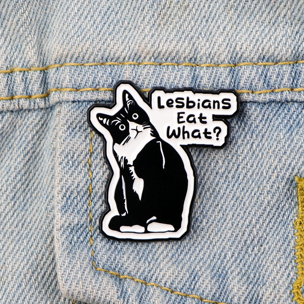 Der Pin zeigt eine detaillierte Katze mit feinen Konturen und der humorvollen Aufschrift „Lesbian eat what?“. Die Oberflaeche ist glatt und glaenzend, was das Katzenmotiv klar und gut sichtbar macht. Der Pin besteht aus einer schwarzen, robusten Metall-Zink-Legierung und hat einen sicheren Verschluss auf der Rückseite, um ihn problemlos an Kleidung oder Accessoires zu befestigen. Ein kleines, stilvolles Accessoire, das Humor und Stil vereint.