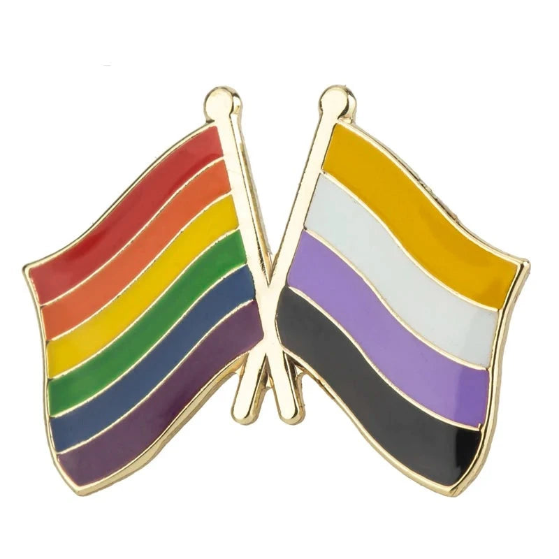 Eine Anstecknadel mit zwei gekreuzten Flaggen: Links die Regenbogenflagge für die LGBTQ+-Community, rechts die Non-Binary-Flagge in Gelb, Weiß, Lila und Schwarz. Goldene Umrandung bietet einen edlen Look.