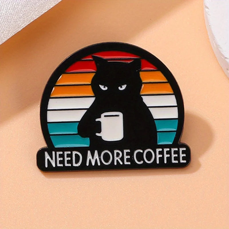 Der Pin zeigt eine Illustration einer schwarzen Katze mit einem grimmigen Gesichtsausdruck, die eine Tasse Kaffee in der Pfote haelt. Im Hintergrund sind horizontale Streifen in warmen Farben (von Rot und Orange oben bis hin zu Blau unten) zu sehen, die an einen Sonnenuntergang erinnern. Unter der Katze steht in dicken weissen Buchstaben der Text „NEED MORE COFFEE“. Die Illustration vermittelt eine Mischung aus Muedigkei