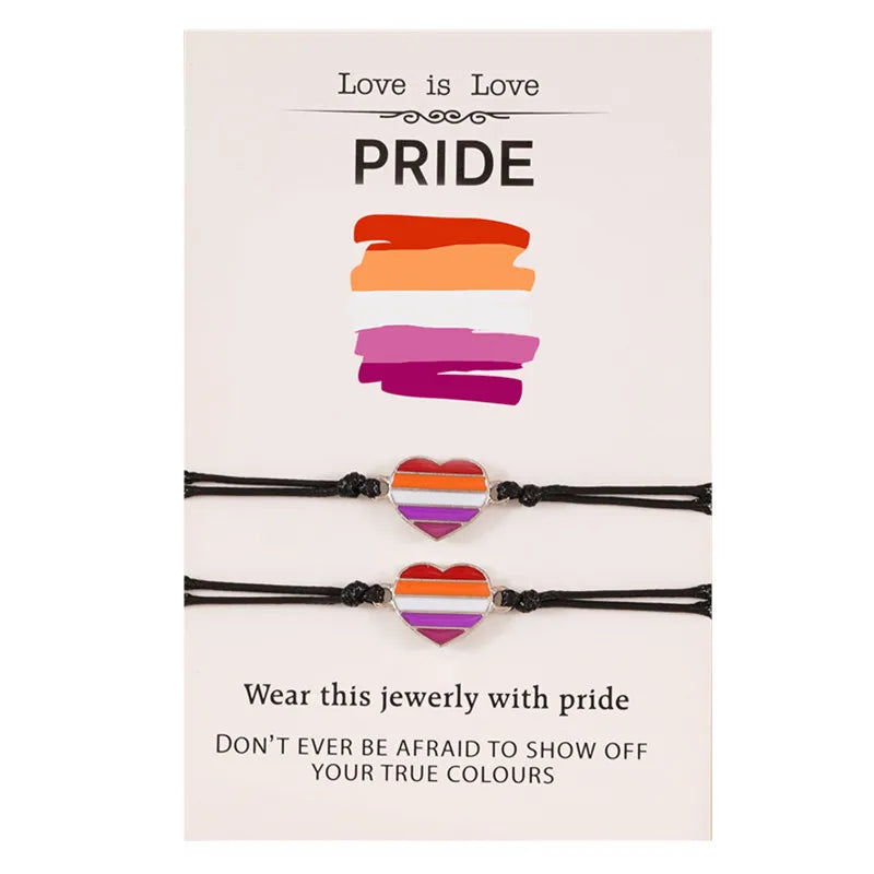 Set aus zwei Armbändern mit Herz-Anhängern in den Farben der lesbischen Pride-Flagge, präsentiert auf einer Karte mit der Aufschrift ‚Love is Love‘ und ‚Pride‘, symbolisch für Stolz und Zugehörigkeit.