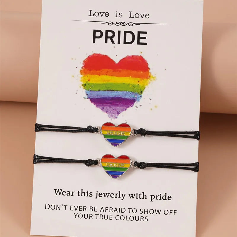 Set aus zwei Armbändern mit Regenbogen-Herz-Anhängern, präsentiert auf einer Karte mit der Aufschrift ‚Love is Love‘ und ‚Pride‘, symbolisch für LGBTQ+ Stolz und Liebe.