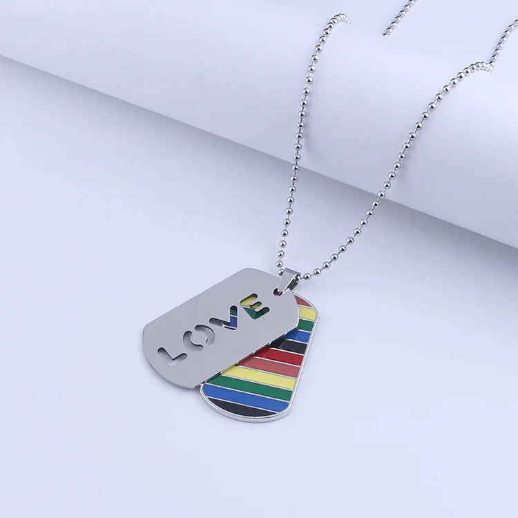 Silberne Halskette mit zwei Anhängern: einer im Regenbogen-Design und einer mit ausgeschnittenem ‚LOVE‘-Schriftzug, symbolisch für LGBTQ+ Stolz und Liebe