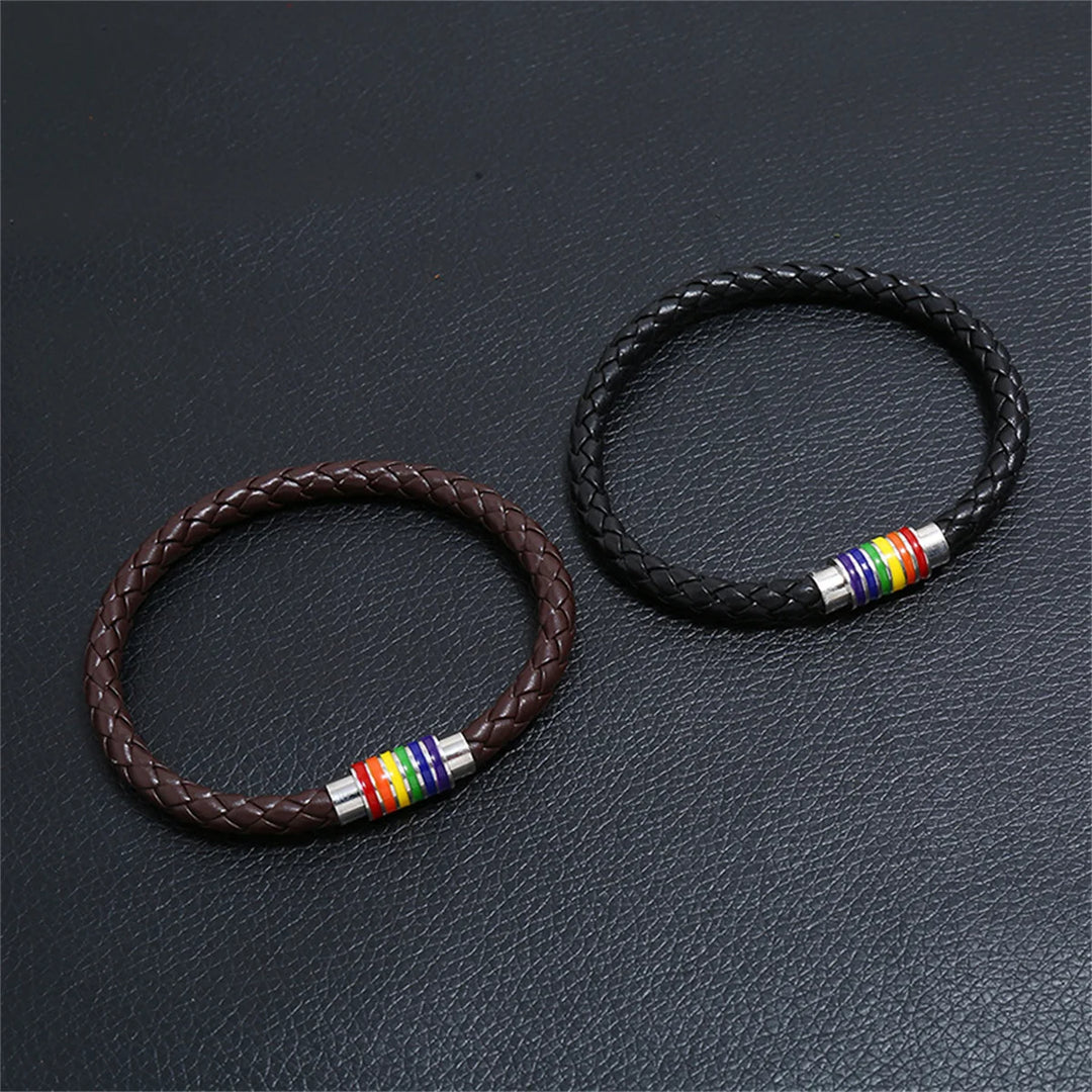 Zwei geflochtene Armbänder aus Leder, eines in Braun und eines in Schwarz, mit silbernen Verschlüssen und Regenbogen-Details, symbolisch für LGBTQ+ Stolz und Vielfalt.