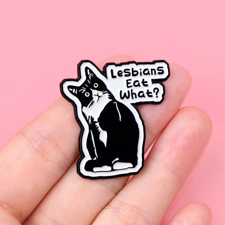 Der Pin zeigt eine detaillierte Katze mit feinen Konturen und der humorvollen Aufschrift „Lesbian eat what?“. Die Oberflaeche ist glatt und glaenzend, was das Katzenmotiv klar und gut sichtbar macht. Der Pin besteht aus einer schwarzen, robusten Metall-Zink-Legierung und hat einen sicheren Verschluss auf der Rückseite, um ihn problemlos an Kleidung oder Accessoires zu befestigen. Ein kleines, stilvolles Accessoire, das Humor und Stil vereint.