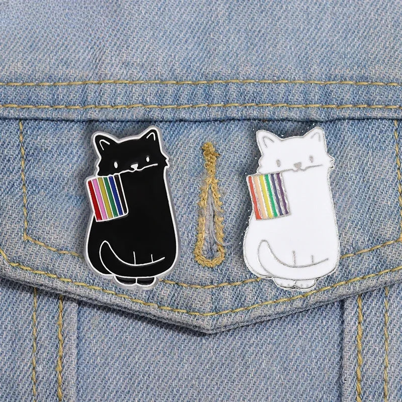 Dieser einzigartige Pin zeigt eine schwarze und eine weisse Katze, die stolz eine LGBTQI+-Regenbogenflagge im Mund tragen. Das Design vereint die kraftvolle Symbolik der Regenbogenflagge mit der geheimnisvollen Eleganz der Katze, wodurch ein ausdrucksstarkes Accessoire entsteht. Perfekt, um an Jacken, Taschen oder Rucksaecken ein Statement für Vielfalt und Akzeptanz zu setzen!