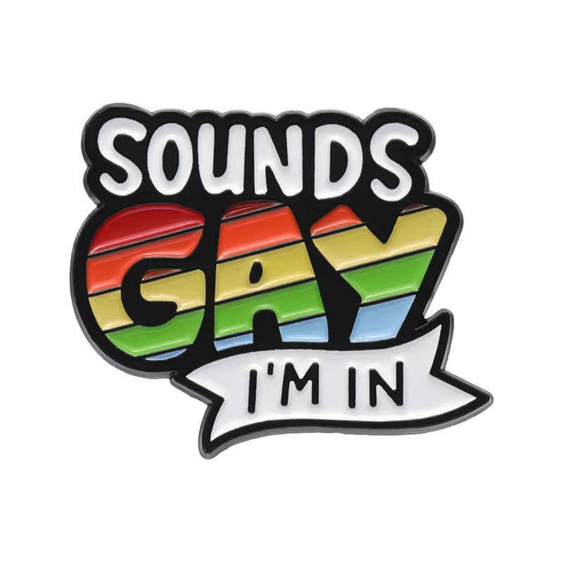 Ein Ansteck-Pin mit dem Text "SOUNDS GAY I'M IN", wobei "GAY" in den Farben der Regenbogenflagge gestaltet ist. Der Pin liegt auf einem hellen Hintergrund.

