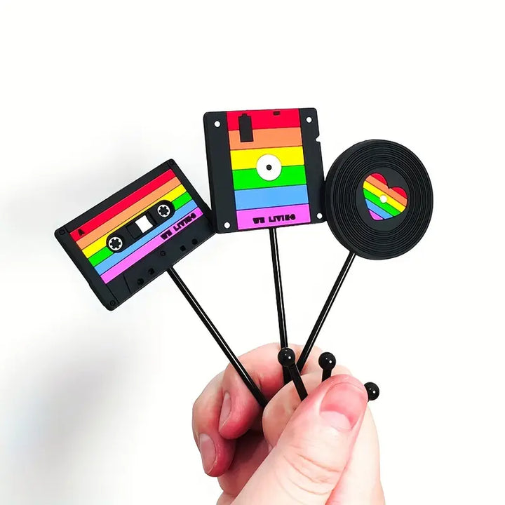 Die drei Wandhaken sind im Retro-Stil gestaltet: einer in Form einer Diskette, einer als Kassette und einer als Schallplatte. Jeder Haken ist bunt in Regenbogenfarben bemalt, was Stolz und Vielfalt symbolisiert.